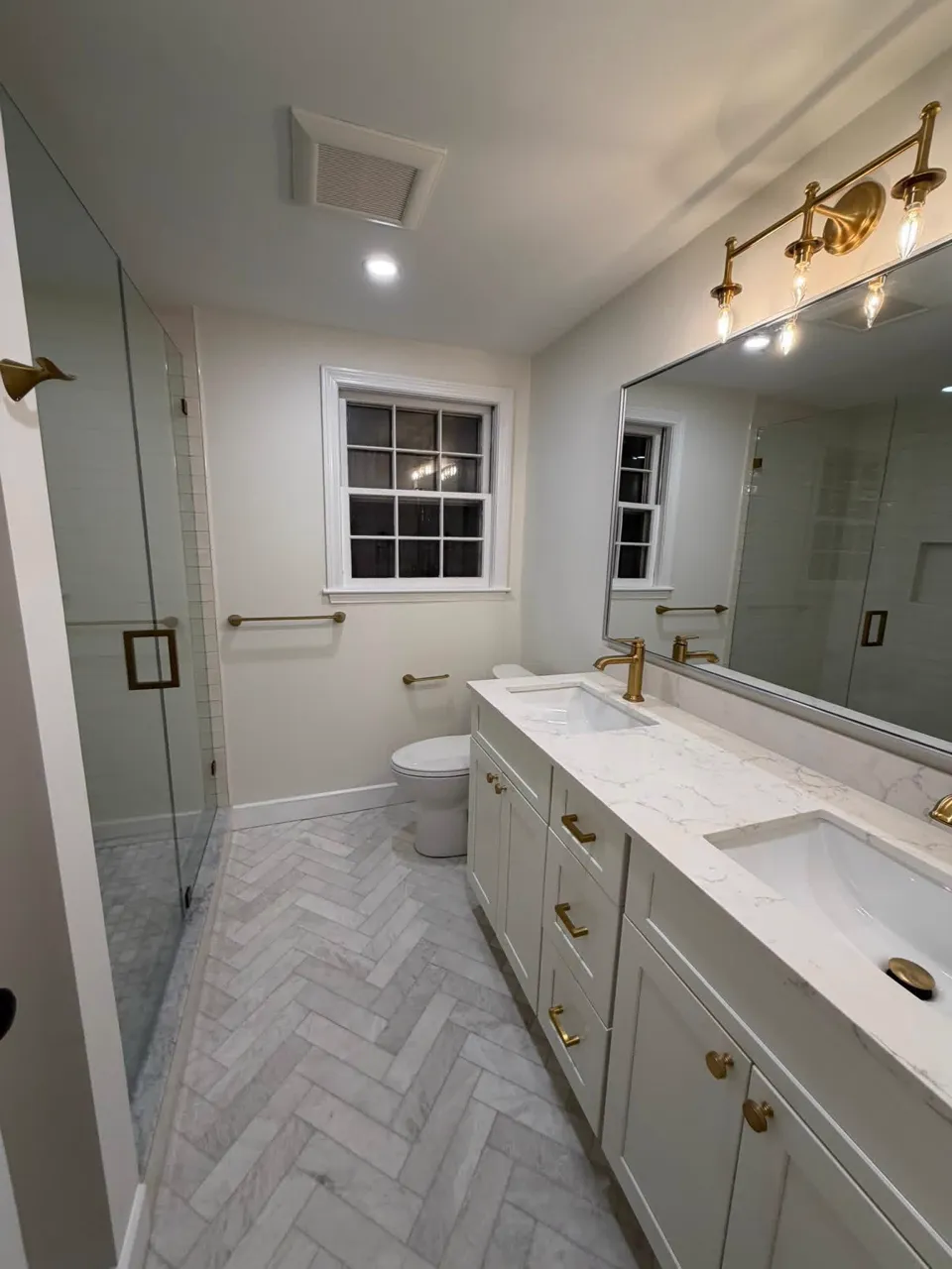 Finished bathroom remodel with glass shower, herringbone marble floor and double vanity