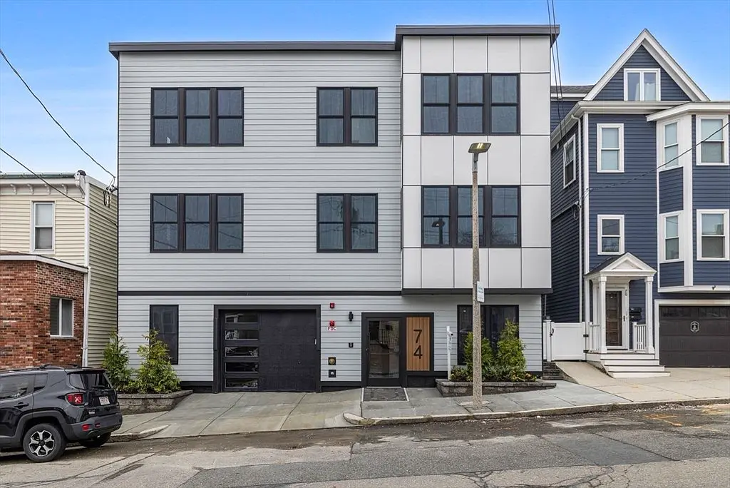 Modern three-story multifamily with light siding, black windows and ground-floor garage