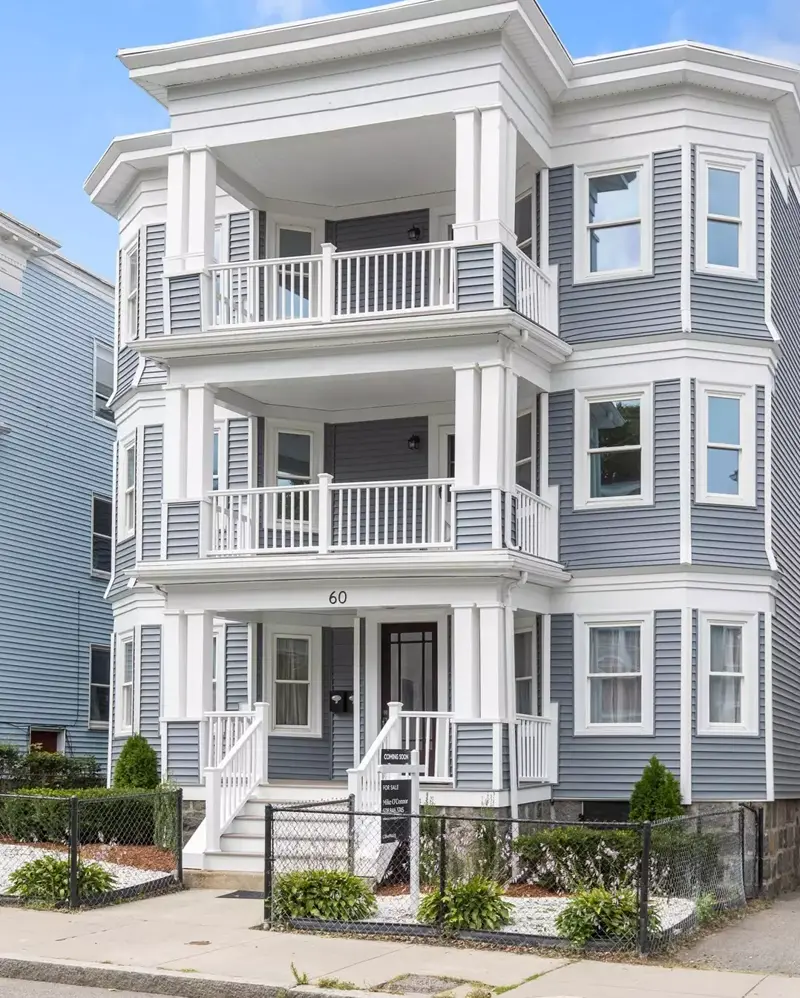 Renovated New England three-family home with stacked white porches, gray siding and new windows